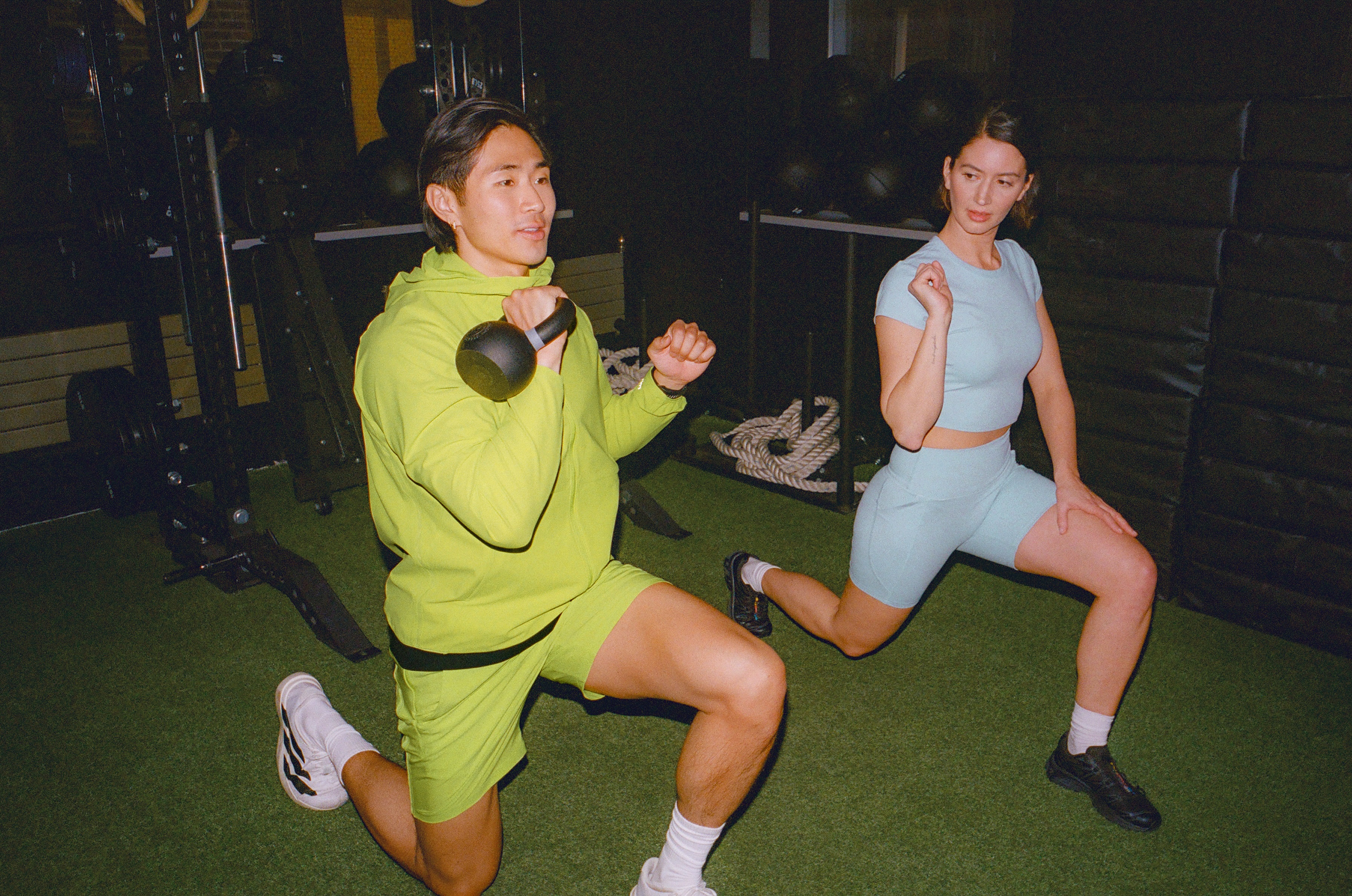 Two people doing lunges in a gym with kettlebells